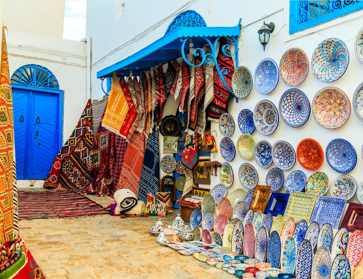 A medina shop front covered in painted ceramic plates and woven rugs beside a blue door