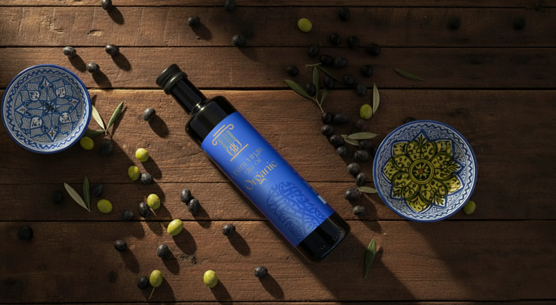 619 Organic Extra Virgin Olive Oil on a dark wooden table scattered with green and black olives and Tunisian ceramic bowls